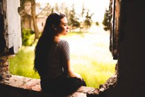 Affascinante giovane donna ammirando la natura seduta in violazione nel muro di edificio abbandonato — Foto stock