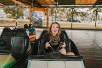 Jovem mulher feliz montando carro pára-choques no parque de diversões se divertindo e olhando para longe — Fotografia de Stock