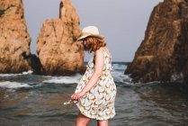 Pretty woman in hat standing and relaxing in the ocean at big rocks — Stock Photo