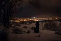 Homem e seu animal de estimação caminham à noite na floresta nevada em um inverno próximo — Fotografia de Stock