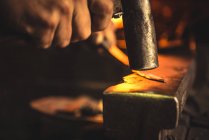 Uomo anonimo che utilizza hummer per forgiare lama da pezzo di metallo in officina professionale — Foto stock