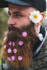 Homem adulto alegre com flores suaves na barba tirando selfie com smartphone na natureza. — Fotografia de Stock