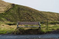 Bon banc de bois debout sur le côté de la route de gravier dans la belle campagne islandaise le jour gris — Photo de stock