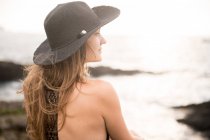 Close-up de jovem mulher de chapéu sentado na costa e olhando para a vista — Fotografia de Stock