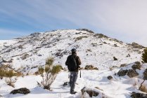 Joven con una mochila de senderismo disfrutando en las montañas nevadas en un día soleado de invierno. - foto de stock