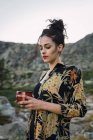 Молодая красивая женщина стоит с кружкой кофе на камнях в сельской местности — стоковое фото
