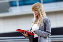 Blonde woman in suit standing on street and using tablet — Stock Photo