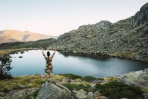 Donna con braccia tese su rocce di piccolo lago in montagna — Foto stock