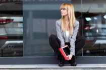 Jovem mulher atraente sentada com tablet na frente do edifício moderno — Fotografia de Stock