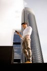 Jovem empresário usando smartphone enquanto está contra arranha-céus na cidade moderna — Fotografia de Stock