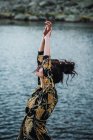 Young woman standing with outstretched arms alone on shore by lake water — Stock Photo