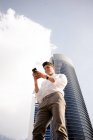 Молодий бізнесмен використовує смартфон, стоячи проти хмарочоса в сучасному місті — стокове фото