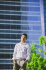Positive young businessman standing against modern building and looking at camera — Stock Photo