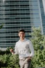 Positiver junger Geschäftsmann steht gegen modernes Gebäude und blickt in die Kamera — Stockfoto