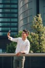 Молодий бізнесмен бере селфі зі смартфоном проти сучасної будівлі — стокове фото