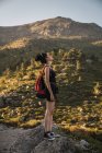 Vista laterale di sottile bella donna con zaino in piedi su rocce nella verde valle godendo della natura con gli occhi chiusi — Foto stock