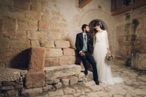 Jeune mariée et marié debout ensemble près du mur — Photo de stock