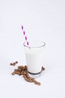 Montón de sabrosas pasas y vaso de leche fresca con paja rayada sobre fondo blanco - foto de stock