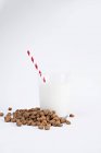 Alça de passas saborosas e copo de leite fresco com palha listrada no fundo branco — Fotografia de Stock