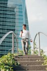 Uomo elegante con smartphone che scende i gradini nella città moderna — Foto stock