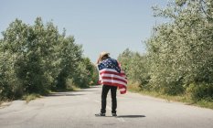 Homme avec drapeau américain marchant sur la route — Photo de stock