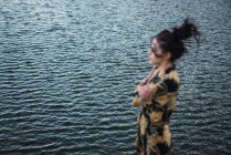 Jovem mulher sozinha na costa, água do lago no fundo — Fotografia de Stock