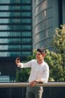 Young businessman taking selfie with smartphone against modern building — Stock Photo