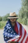 Man happy and jumping for joy with an American flag on a lonely road — Stock Photo