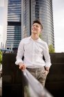 Smiling young businessman in elegant outfit smiling while standing near railing on street of modern city — Stock Photo