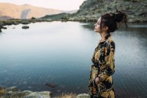 Young brunette woman on rocks of small lake in mountains — Stock Photo