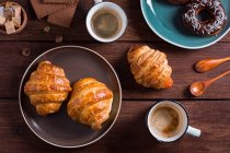 De xícaras acima de café e croissants na chapa na mesa de madeira . — Fotografia de Stock