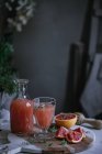 Jus de pamplemousse frais en verre et bouteille avec ingrédient sur la table de cuisine — Photo de stock