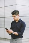 Eleganter Mann benutzt Handy, während er gegen Hauswand steht — Stockfoto