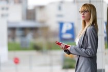 Giovane donna d'affari attraente in piedi con tablet sulla strada su sfondo sfocato — Foto stock