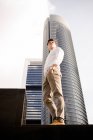 Confident young man standing near tower building with hands in pockets — Stock Photo