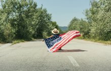 Homem com bandeira americana sentado na estrada — Fotografia de Stock