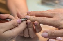 Female manicurist cutting nails of client with nail tongs in beauty salon — Stock Photo