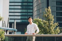 Giovane uomo d'affari sorridente in piedi vicino ringhiera contro edificio moderno — Foto stock