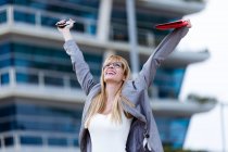 Young excited businesswoman standing with arms up against office building — Stock Photo