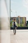Молодой мужчина в стильном наряде с помощью смартфона во время прогулки по тротуару возле здания на городской улице — стоковое фото