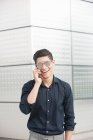 Jovem empresário alegre falando ao telefone contra a parede do prédio — Fotografia de Stock