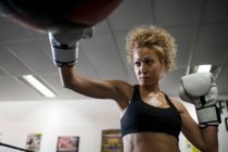 Серйозна жінка тренується в тренажерному залі з мішком для ударів — стокове фото