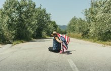Homme avec drapeau américain assis sur la route — Photo de stock