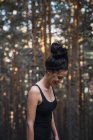 Bella giovane donna in canotta ridere e guardando giù mentre in piedi nel bosco — Foto stock
