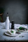 Blauschimmelkäse mit Kräutern in weißer Schale steht auf einem Marmortisch mit Gefäßen und weißem Textilmaterial im weichen Fokus — Stockfoto