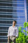Позитивный молодой бизнесмен стоит против современного здания и смотрит в камеру — стоковое фото