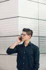 Young businessman speaking on phone against building wall — Stock Photo