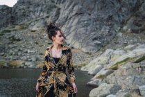 Giovane donna in piedi da sola sulla riva rocciosa del lago — Foto stock