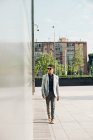 Hombre elegante y seguro en gafas de sol caminando en la ciudad - foto de stock