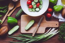 De arriba surtido de verduras maduras rojas y verdes, ensalada en cuenco y tabla de cortar de madera . - foto de stock